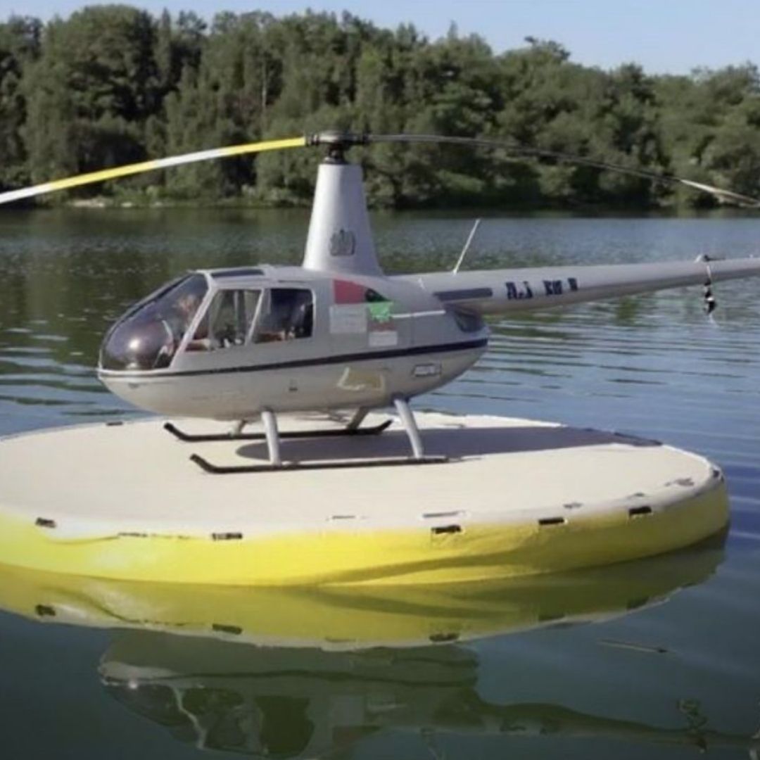 A small grey helicopter resting securely on a white and yellow inflatable Hardline Helipad, demonstrating its aquatic deployment capability